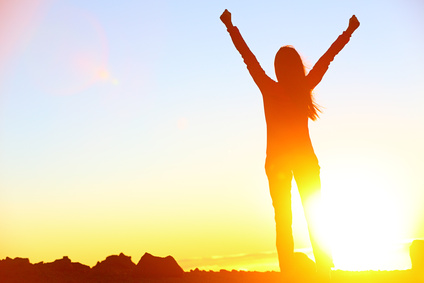 Happy celebrating winning success woman at sunset or sunrise standing elated with arms raised up above her head in celebration of having reached mountain top summit goal during hiking travel trek.